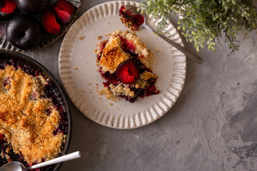 fresh made plum crumble on white plate on grey background. top view