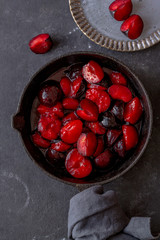 red ripe caramelised plums in cast iron on dark background. top view