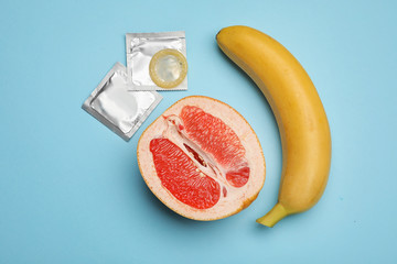 Condoms with banana and cut grapefruit on light blue background, flat lay. Safe sex
