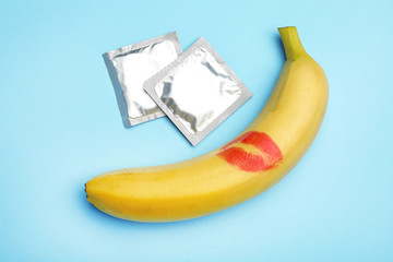 Condoms and banana with lipstick kiss mark on light blue background, flat lay. Safe sex