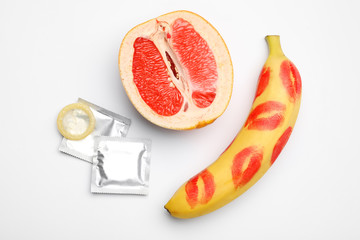 Condoms, cut grapefruit and banana with lipstick kiss marks on white background, flat lay. Safe sex