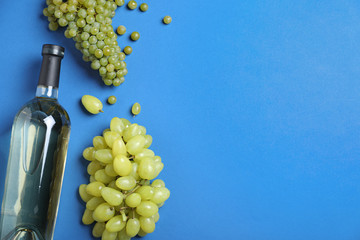 Fresh ripe juicy grapes and bottle of wine on blue background, flat lay. Space for text