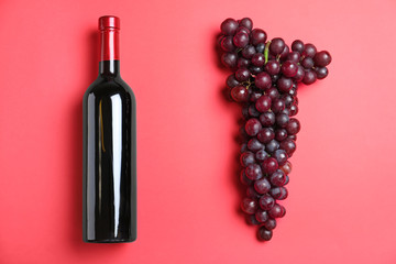 Fresh ripe juicy grapes and bottle of wine on red background, flat lay