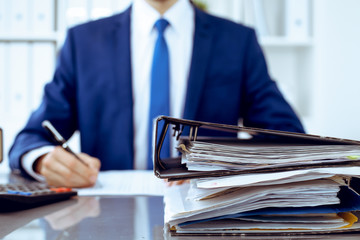 Binders with papers waiting to be processed with businessman or bookkeeper back in blur. Accounting...