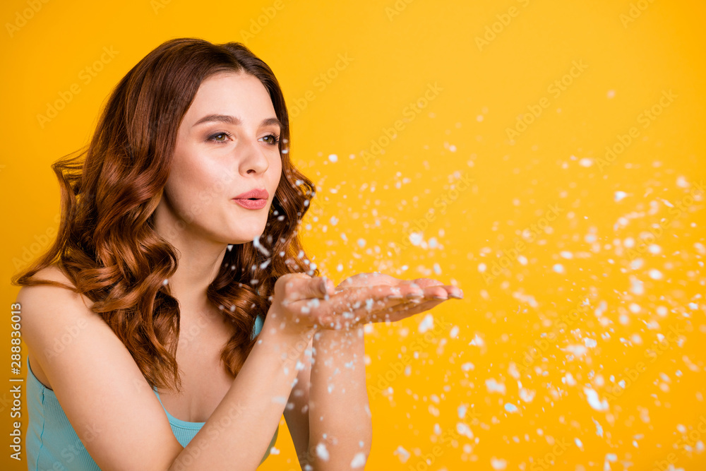 Poster Close up turned photo of trendy charming cute sweet lovely pretty girlfriend blowing white snowflakes like confetti wearing teal tank-top while isolated over yellow vibrant color background