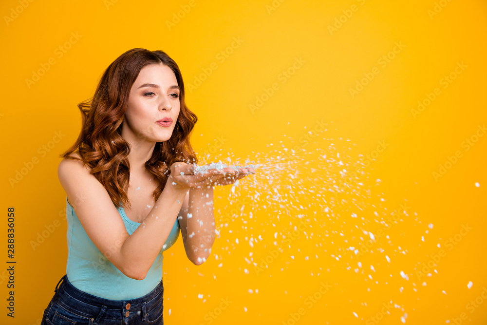 Sticker Turned copyspace photo of lovely hipster millennial youngster girlfriend blowing white snowflakes away from her hands wearing teal singlet jeans denim isolated with yellow background vivid color