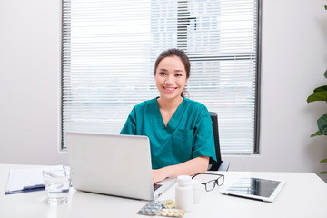 Young woman doctor at work while typing on laptop computer in hospital office.