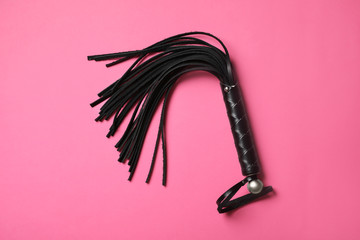 Black whip on pink background, top view. Accessory for sexual role play