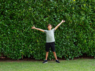 teenager stands on a background of green hedges.