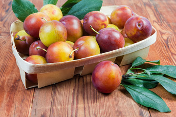 Plums with leaves in wooden basket on rustic table