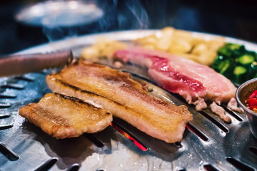 Close up raw sliced pork on hot pan with smoke Korean-Style BBQ in a Korean restaurant. Traditional Korean food.