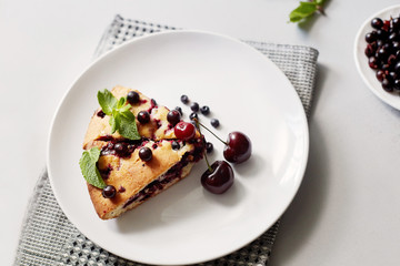 Piece of pie with blueberries, rasberry,cherries and mint for dessert on a white plate, napkin. Pieces of delicious homemade cake
