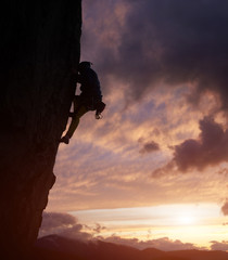 Male climber silhouette overcoming difficult path to top on challenging cliff in nightfall. Rock climbing. Cloudy sky with cumulonimbus over mountain peaks on background. Low angle view. Copy space