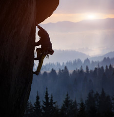 Silhouette of man rock climbing on straight vertical rock at sunrise. Sunlight covering mountains...