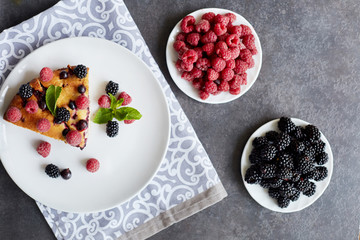Piece of pie with blueberries, rasberry and mint for dessert on a white plate, napkin. Pieces of delicious homemade cake on a background