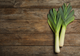 Fresh raw leeks on wooden table, flat lay with space for text. Ripe onion