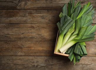 Crate of fresh raw leeks on wooden table, top view with space for text. Ripe onion