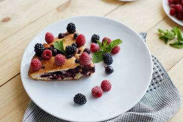 Piece of pie with blueberries, rasberry and mint for dessert on a white plate, napkin. Pieces of delicious homemade cake on a wooden boards background