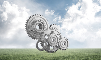 Abstract mechanism with cogwheels on green meadow