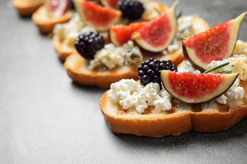 Bruschettas with cheese, figs and blackberries on grey table, closeup