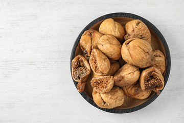 Wooden bowl of tasty dried figs on white table, top view. Space for text