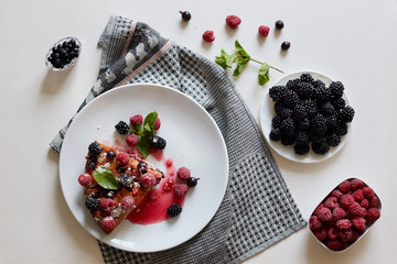 Piece of pie with blueberries, rasberry and mint for dessert on a white plate, napkin. Pieces of delicious homemade cake on a wooden boards background