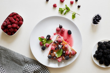 Piece of pie with blueberries, rasberry and mint for dessert on a white plate, napkin. Pieces of delicious homemade cake on a wooden boards background