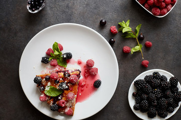 Piece of pie with blueberries, rasberry and mint for dessert on a white plate, napkin. Pieces of delicious homemade cake on a wooden boards background