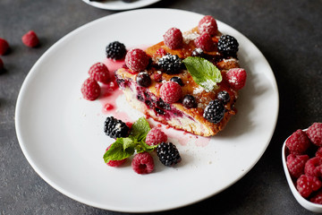 Piece of pie with blueberries, rasberry and mint for dessert on a white plate, napkin. Pieces of delicious homemade cake on a wooden boards background