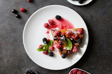 Piece of pie with blueberries, rasberry and mint for dessert on a white plate, napkin. Pieces of delicious homemade cake on a wooden boards background
