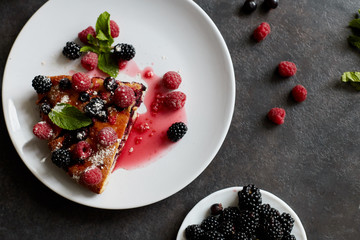 Piece of pie with blueberries, rasberry and mint for dessert on a white plate, napkin. Pieces of delicious homemade cake on a wooden boards background
