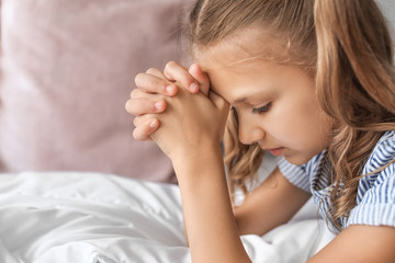 Cute little girl praying in bedroom