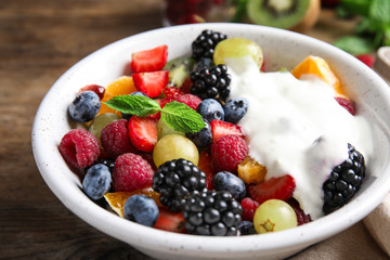 Fresh tasty fruit salad with yogurt on wooden table, closeup