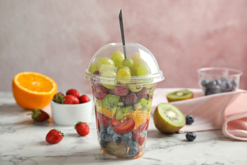 Fresh tasty fruit salad in plastic cup on white marble table