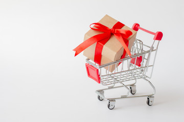 Gift box on miniature shopping cart on white background. Christmas and happy new year concept.