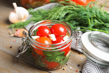 Pickled tomatoes in glass jar and products on wooden table