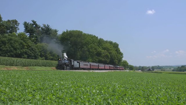 A 1924 Steam Engine with Passenger Train Puffing Smoke Traveling Along the Amish Countryside on a Summer Day