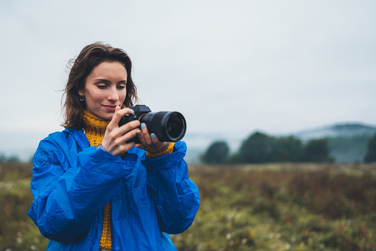 photographer tourist girl in blue raincoat hold in hands photo camera take photography foggy mountain, traveler shooting autumn nature, click technology, landscape vacation concept free space