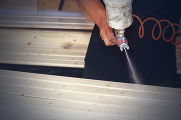 A man covers wooden boards with varnish in the workshop with a spray.