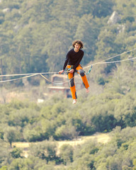 A man is walking along a stretched sling. Highline in the mountains. Man catches balance. Performance of a tightrope walker in nature. Highliner on the background of valley.