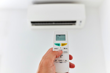 Modern air conditioner unit with a hand holding a remote.