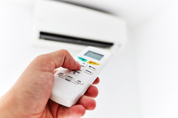 Modern air conditioner unit with a hand holding a remote.