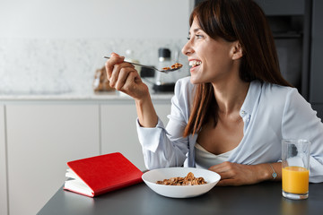 Positive optimistic cheery woman indoors at home at the kitchen have a breakfast eat corn flakes.