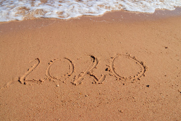 Concept of Christmas and New Year's holidays at tropical resort. 2020 number written on wet sand of sea beach