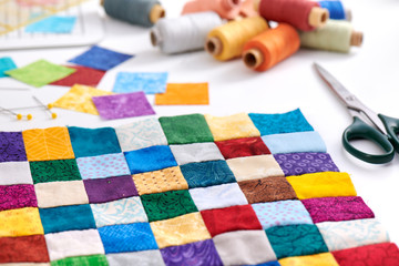 Colorful part of quilt sewn from square pieces, spools of thread, scissors, quilting and sewing accessories - obrazy, fototapety, plakaty