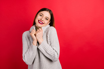 Pretty overjoyed lady touching hands soft knitted sweater isolated on red background