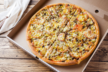 Freshly baked pizza in a cardboard box on a wooden table.