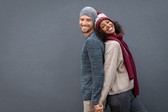 Happy couple in winter clothes leaning against back