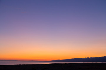 Fototapeta premium Dawn on a lake in the mountains. rays of the rising sun, orange color. Kyrgyzstan, Issyk-Kul Lake. Bright sky, background in warm colors.