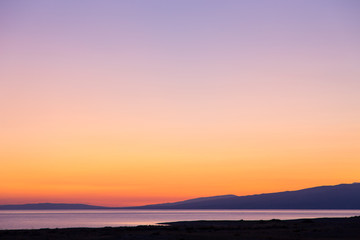 Dawn on a lake in the mountains. rays of the rising sun, orange color. Kyrgyzstan, Issyk-Kul Lake. Bright sky, background in warm colors.